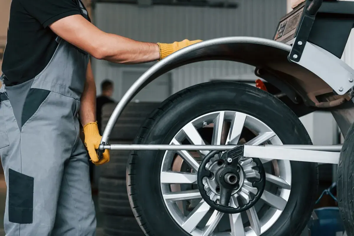 Mechanik w żółtych rękawiczkach dokonuje doważania kół na samochodzie, dbając o płynną jazdę.