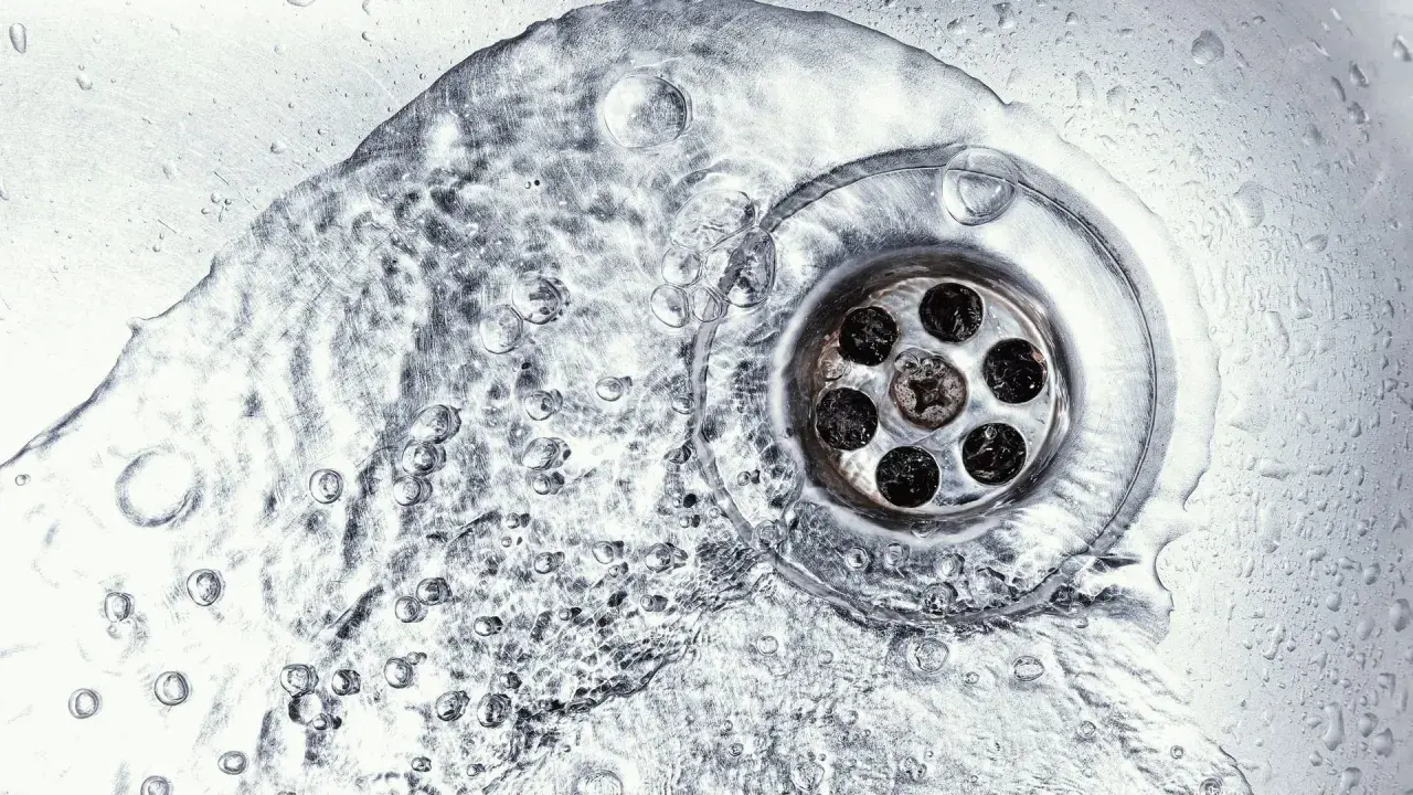 Wasser fließt in einen verstopften Abfluss. Vielleicht hilft ein Gebissreiniger, die Ablagerungen zu lösen.
