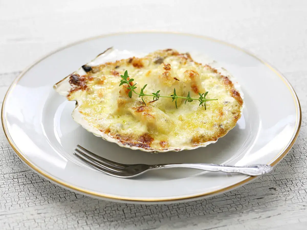 Deliciosas vieiras gratinadas en su concha, cubiertas de queso derretido y doradas, adornadas con una ramita de tomillo.