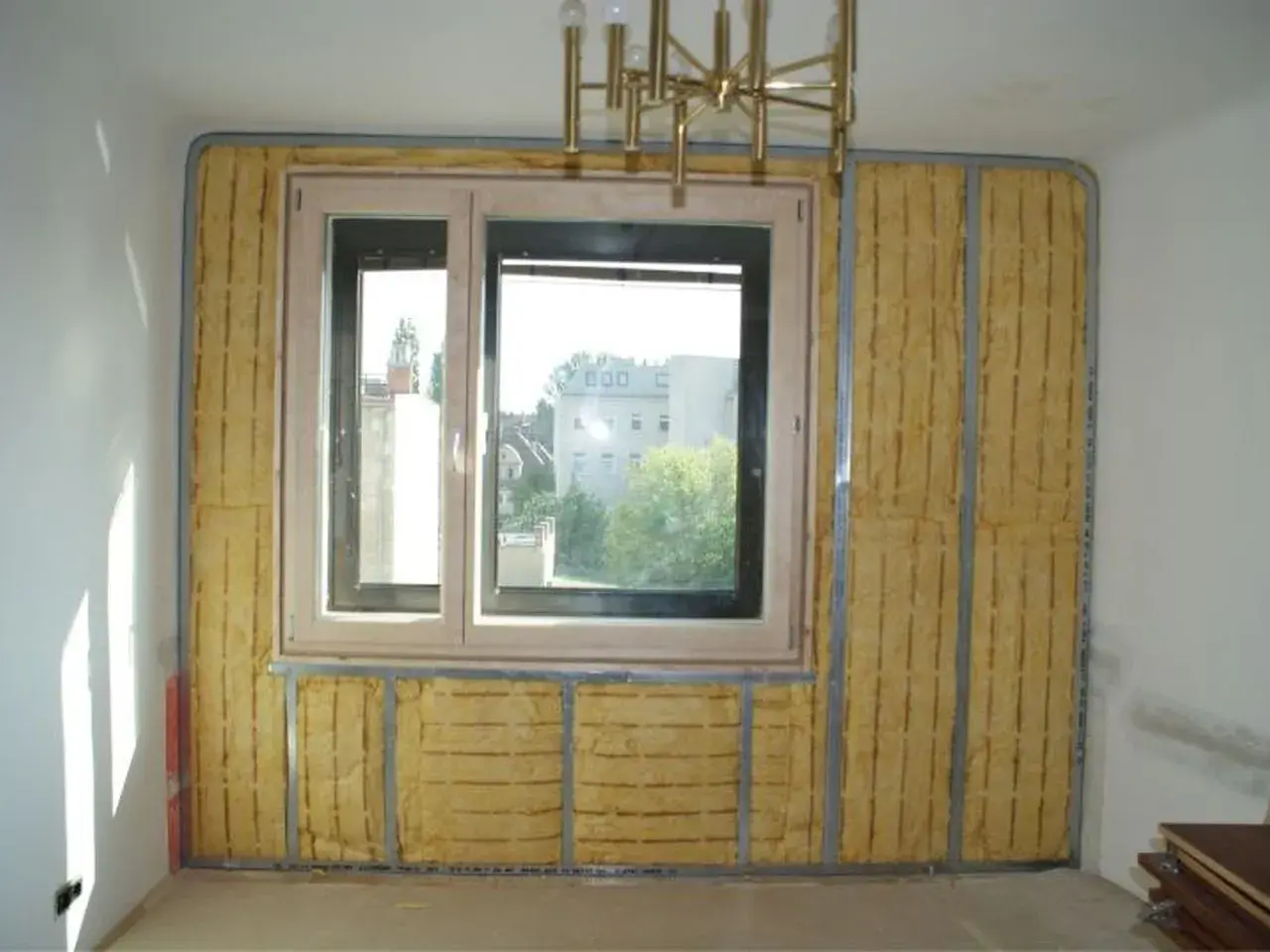 Izolacja akustyczna wokół okna, z widocznym materiałem w kolorze piaskowym na ścianie, przygotowana do dalszych prac wykończeniowych.