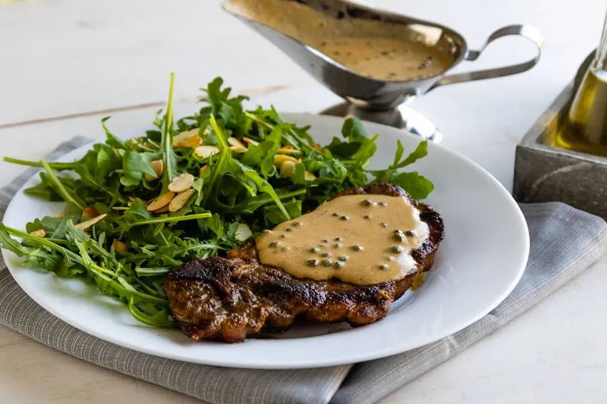 Un succulento filetto al pepe verde, nappato con salsa cremosa, servito con un'insalata fresca di rucola e mandorle.