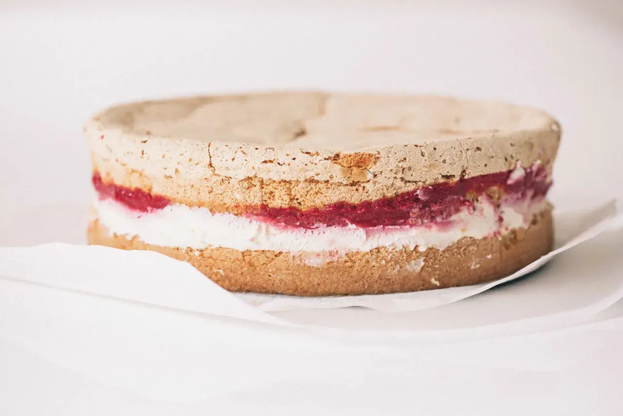 Himbeertorte rezept: Ein Biskuitboden mit Himbeermarmelade und Sahne, bereit zum Verzieren.