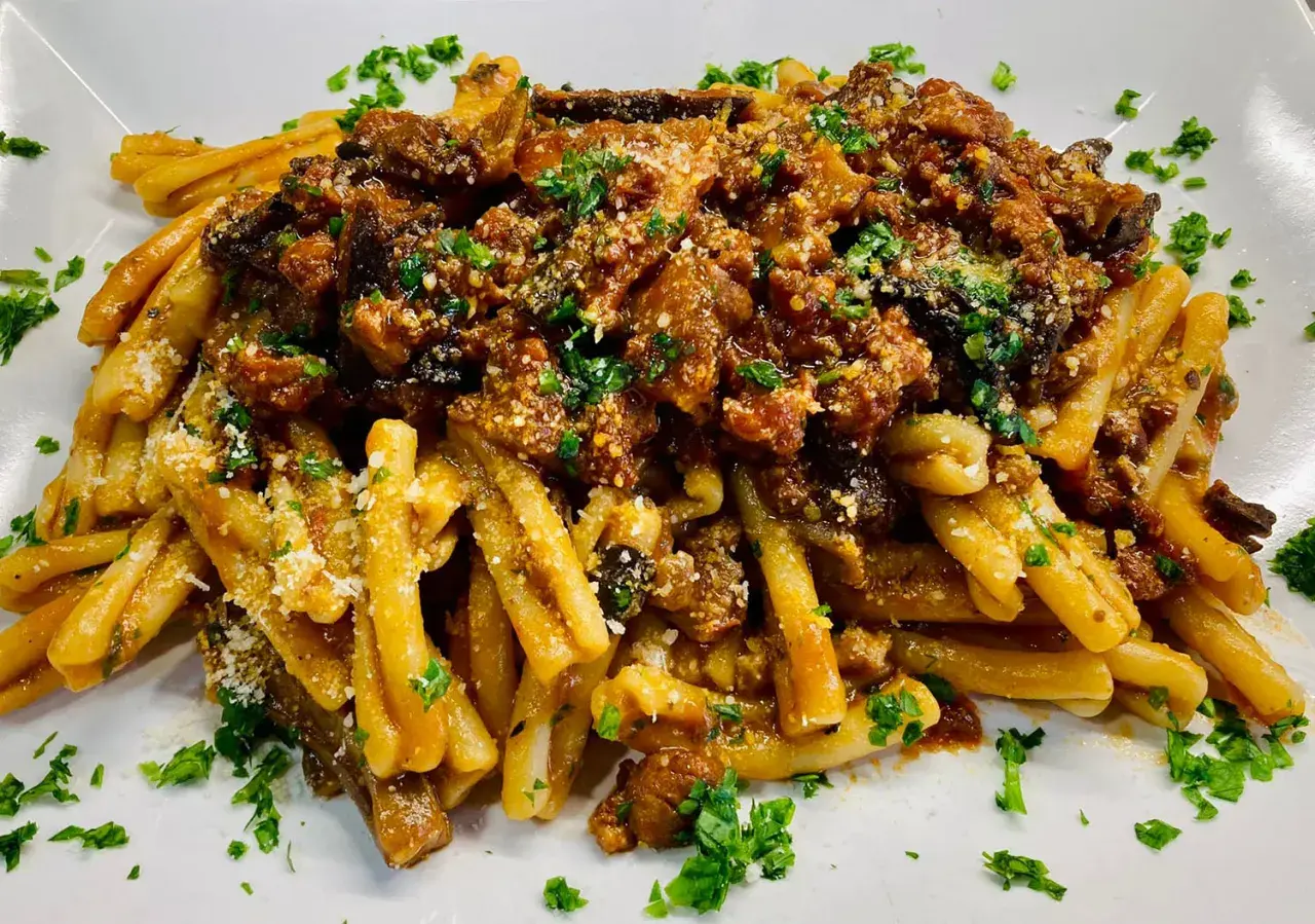 Un piatto di pasta alla norma fumante, con melanzane fritte, pomodoro e ricotta salata grattugiata, guarnito con prezzemolo fresco.