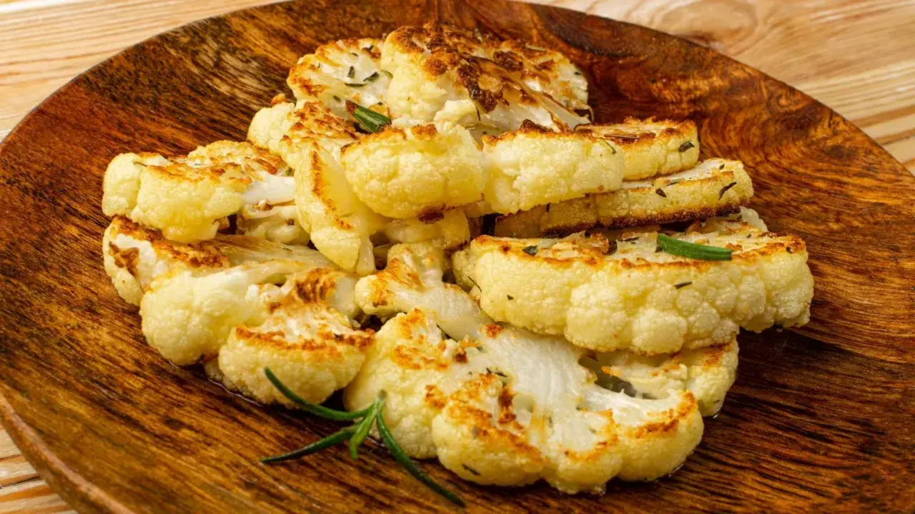 Tranches de chou-fleur rôti, dorées et garnies d'herbes, servies sur un plat en bois.