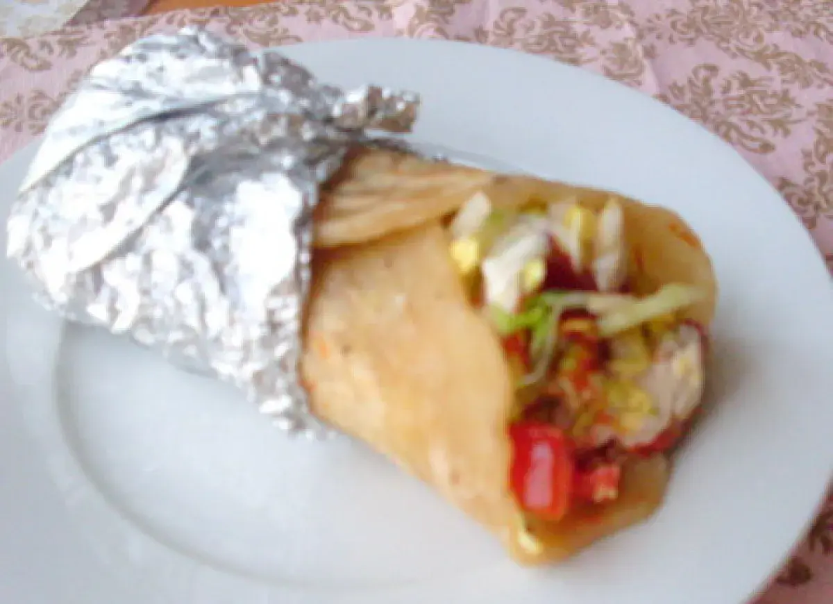 Pyszny placek z kebabem, zawinięty w folię aluminiową, z widocznym nadzieniem z warzyw i mięsa.