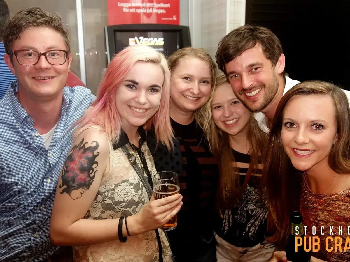 Glada vänner på en pub crawl i Stockholm. En kvinna med rosa hår håller ett glas öl.