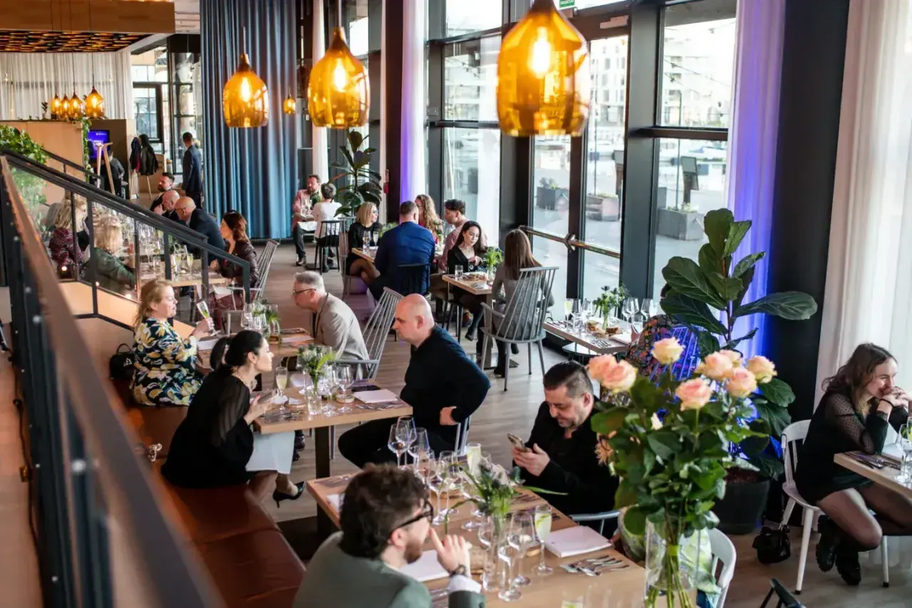 W restauracji "Polskie Smaki" goście delektują się posiłkami przy elegancko nakrytych stołach, w otoczeniu nowoczesnego wystroju i ciepłego światła.
