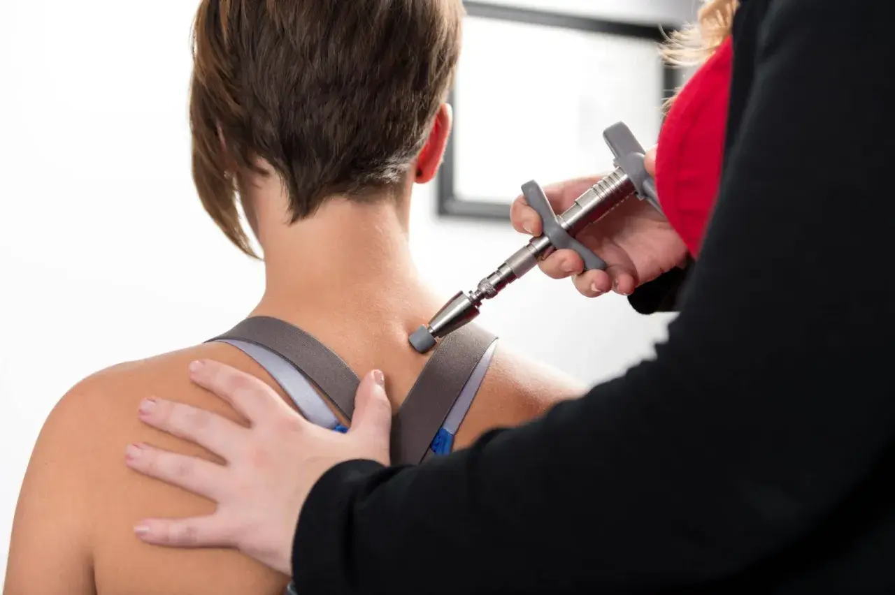 Thérapeute utilisant un appareil pour soulager la douleur haut du dos gauche d'une patiente.