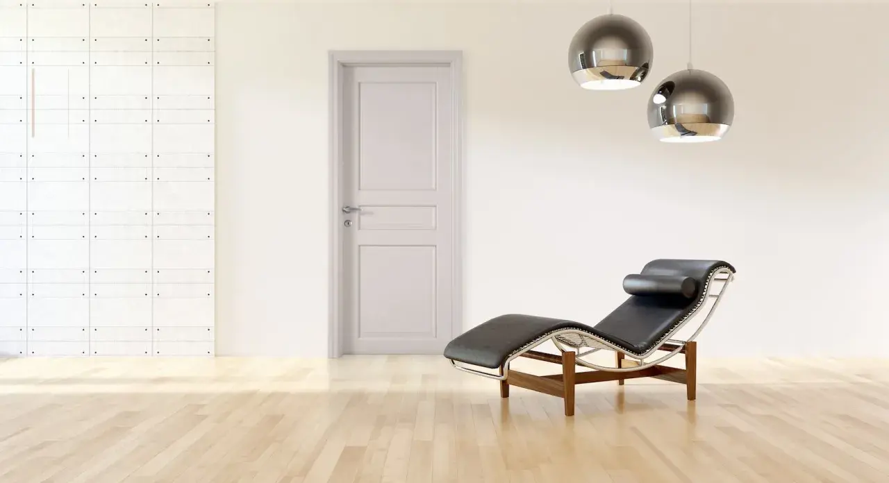 Un ambiente minimalista con porte bianche, pareti tortora, una chaise longue in pelle nera e due lampade a sospensione sferiche.