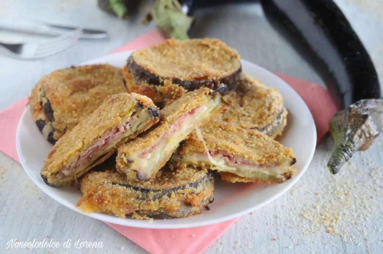 Cordon bleu di melanzane impanati e fritti, ripieni di prosciutto e formaggio filante, serviti su un piatto bianco.