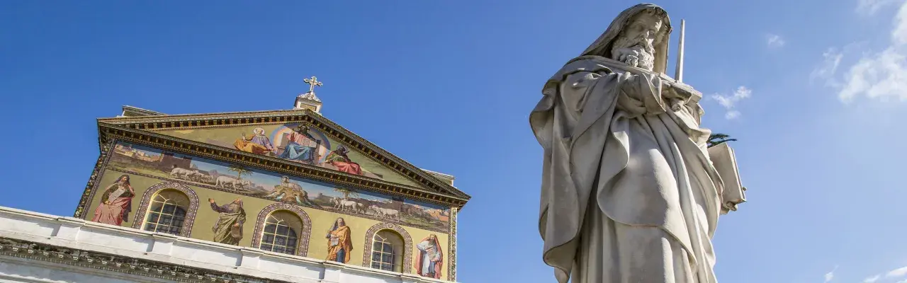 Statua imponente e facciata decorata con mosaici a San Paolo fuori le Mura. Curiosità: ogni mosaico racconta una storia biblica.