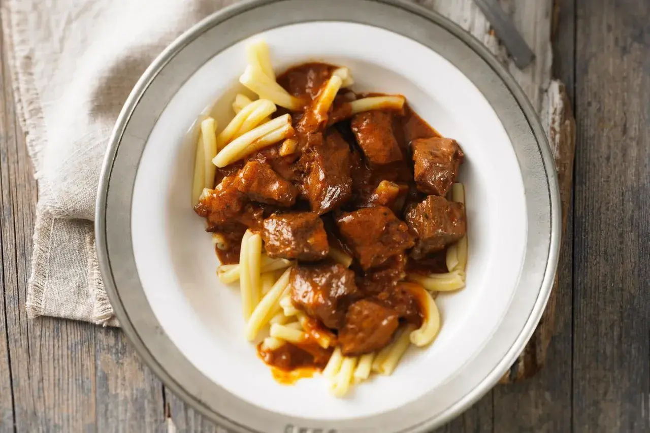 Herzhaftes Gulasch mit zarten Fleischstücken in würziger Sauce, serviert auf hellen Nudeln. Ein Klassiker, der zeigt, was ist Gulasch.