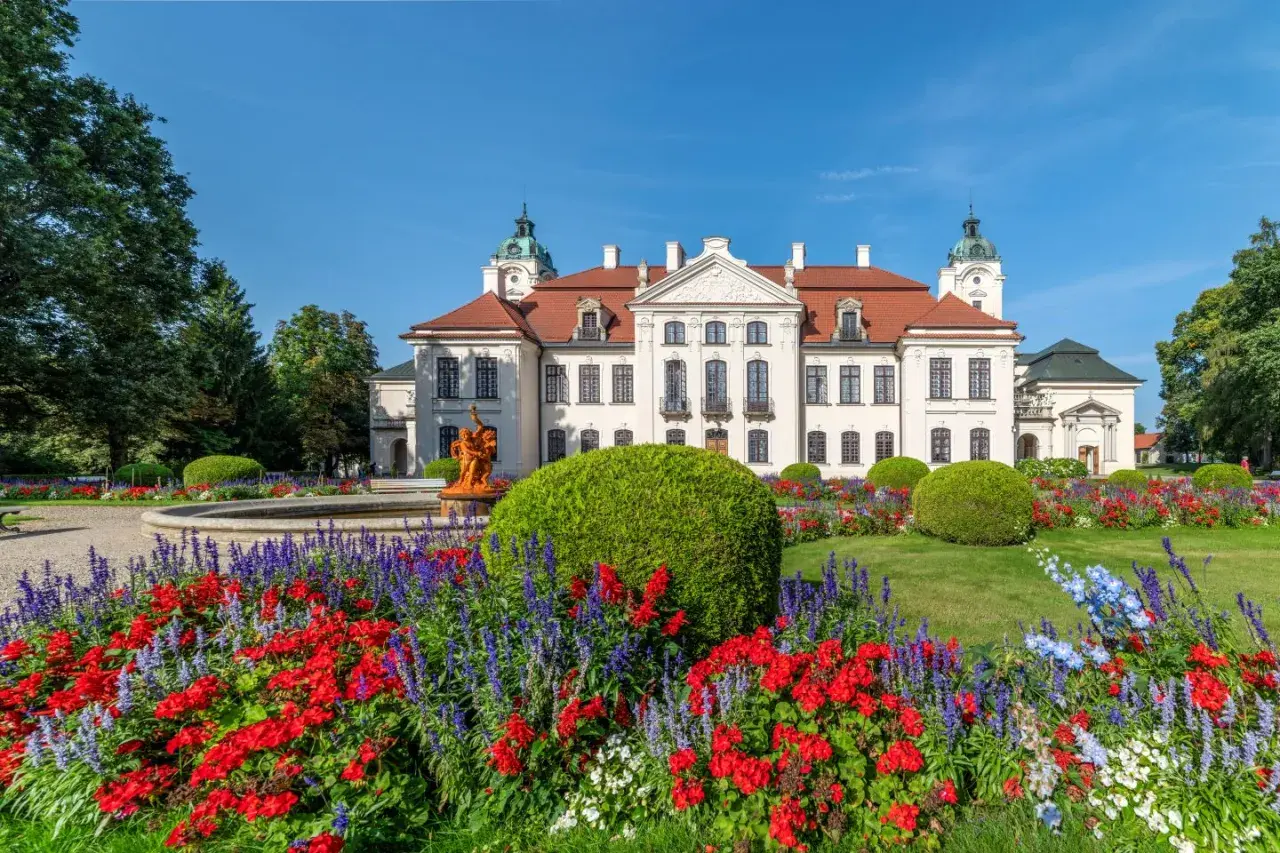 Pałac Zamoyskich w Kozłówce otoczony kwitnącym ogrodem z fontanną i rzeźbą.