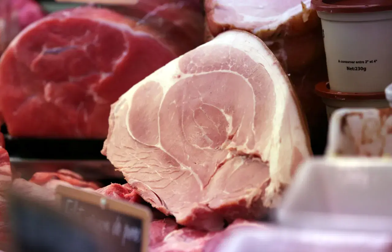 Gros plan sur une pièce de viande rose pâle, probablement une côte de porc, avec des marbrures de gras. Derrière, on aperçoit de la viande rouge vif.