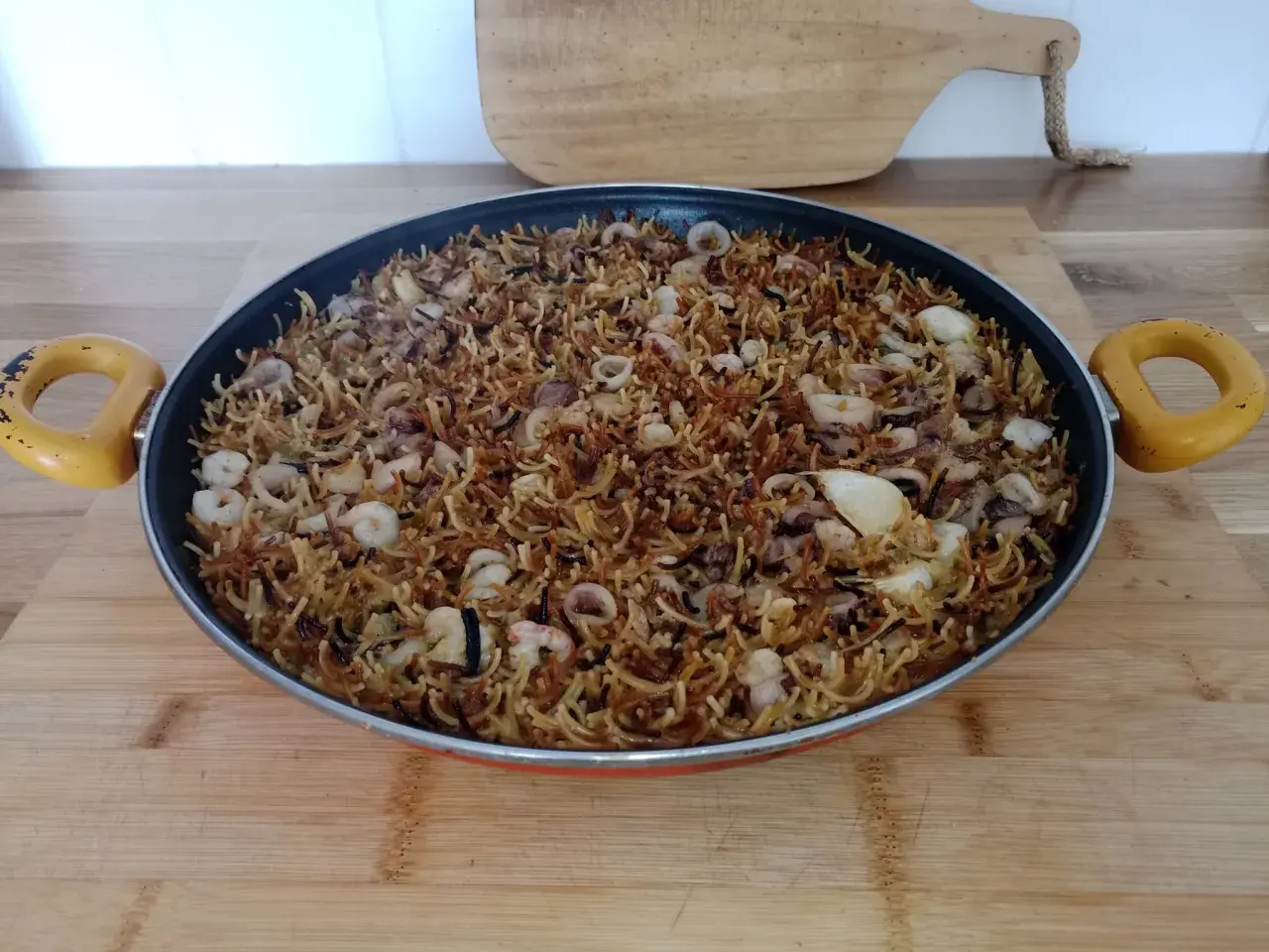 Fideos fideuá con calamares y gambas, listos para servir en una paellera.