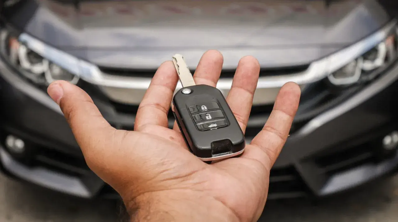 Mano che tiene una chiave auto moderna, pronta per duplicare la chiave auto. Auto scura sullo sfondo.