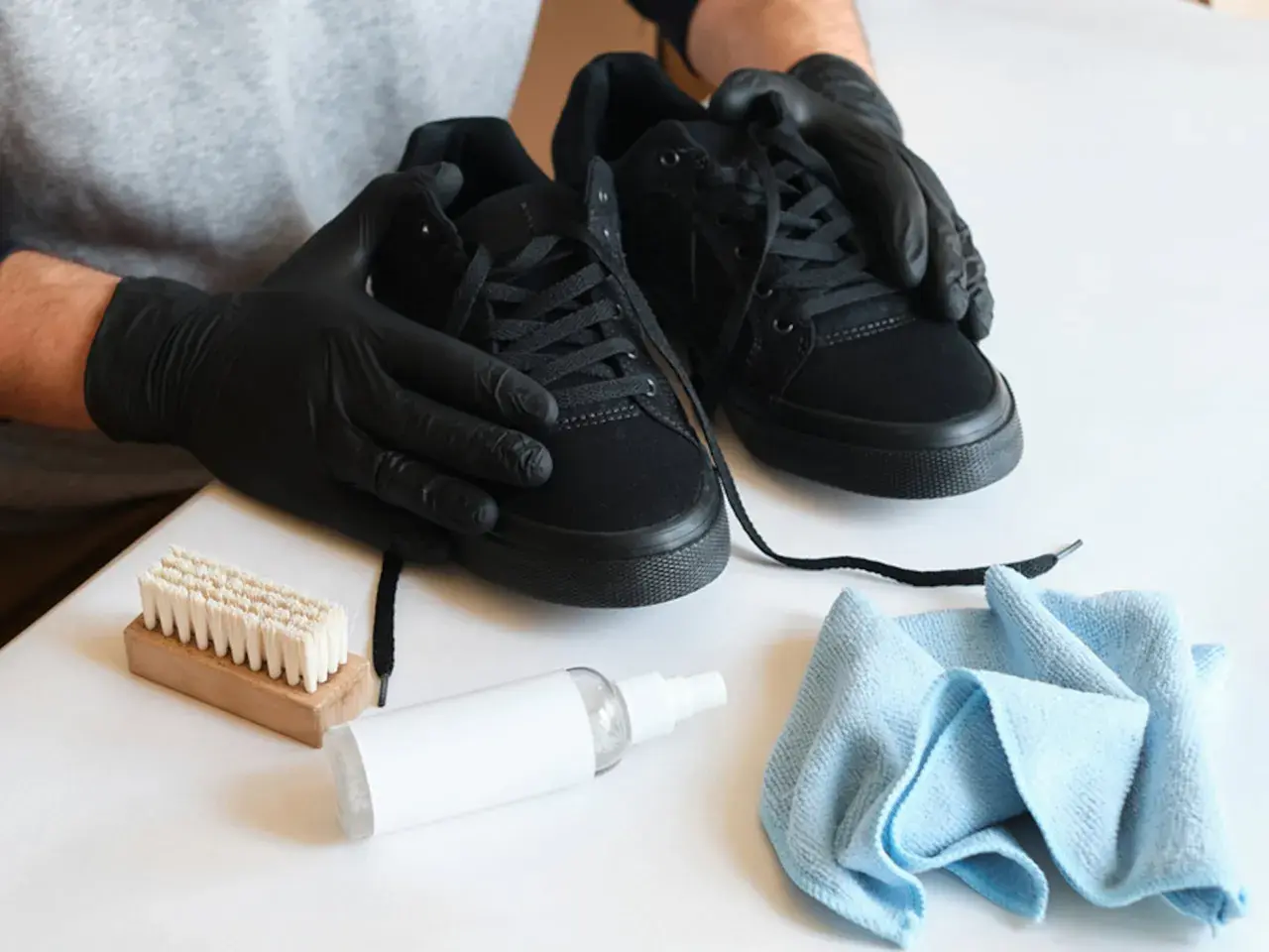 Manos enguantadas limpian zapatos negros con cepillo y spray.
