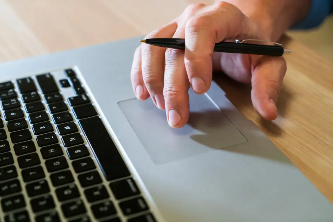 Mano con bolígrafo sobre el touchpad de un portátil, como si buscara qué es un hash.