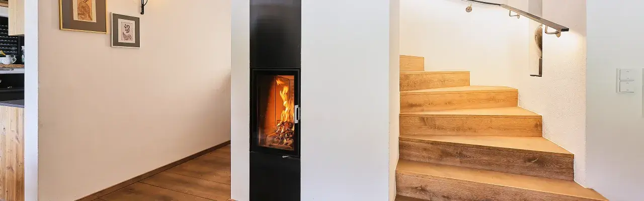 Ein moderner Kamin mit brennendem Feuer, daneben eine Holztreppe. Hier sieht man, was ein Grundofen leisten kann: Wärme und Gemütlichkeit.