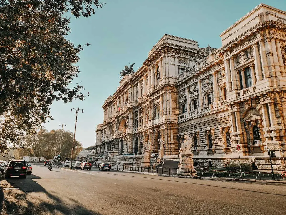 Edificio imponente su via dei Cosmati, con auto che transitano e un albero ombroso.
