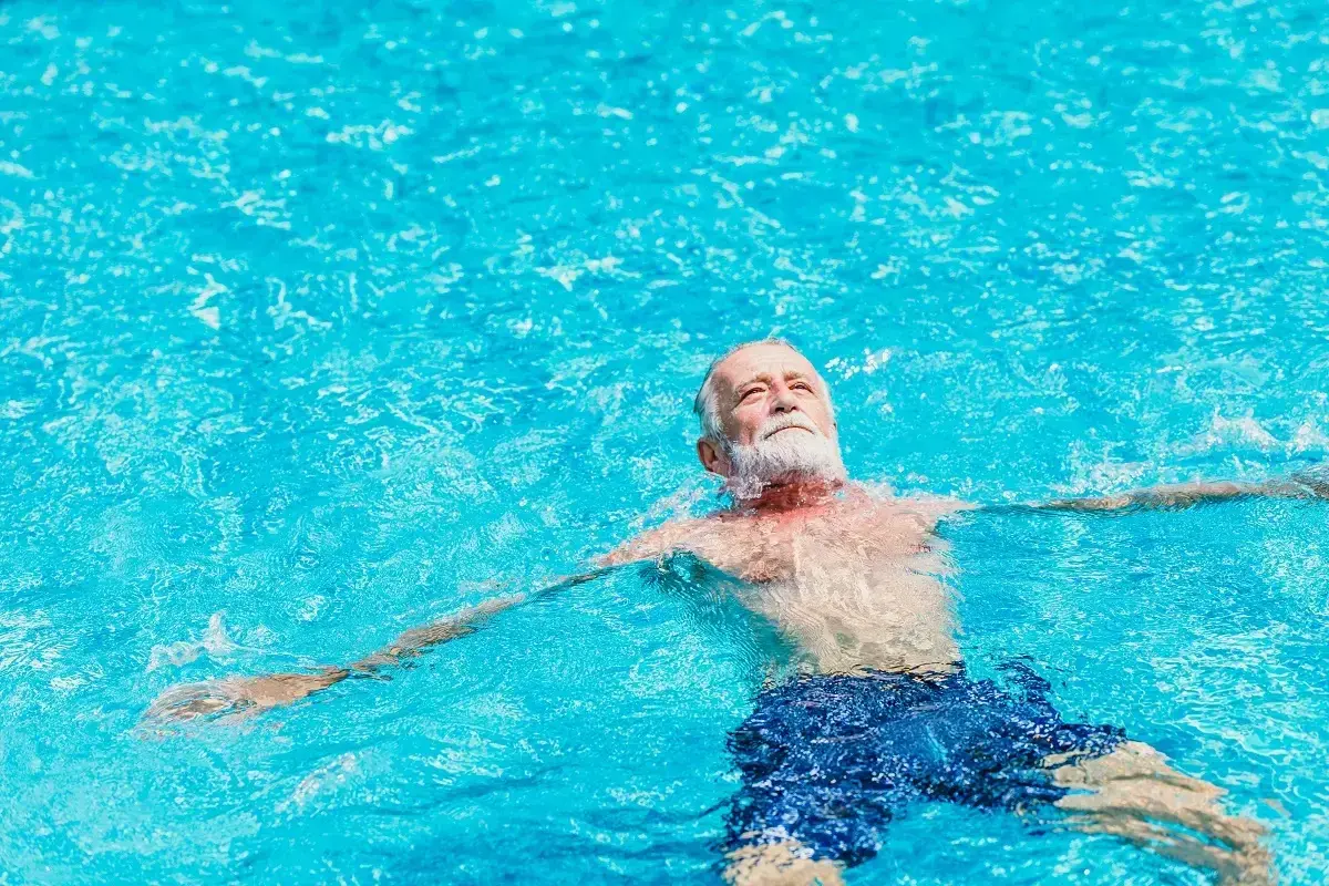 Ein älterer Mann mit Bart entspannt sich im Wasser. Schwimmen bei Arthrose kann Linderung verschaffen.