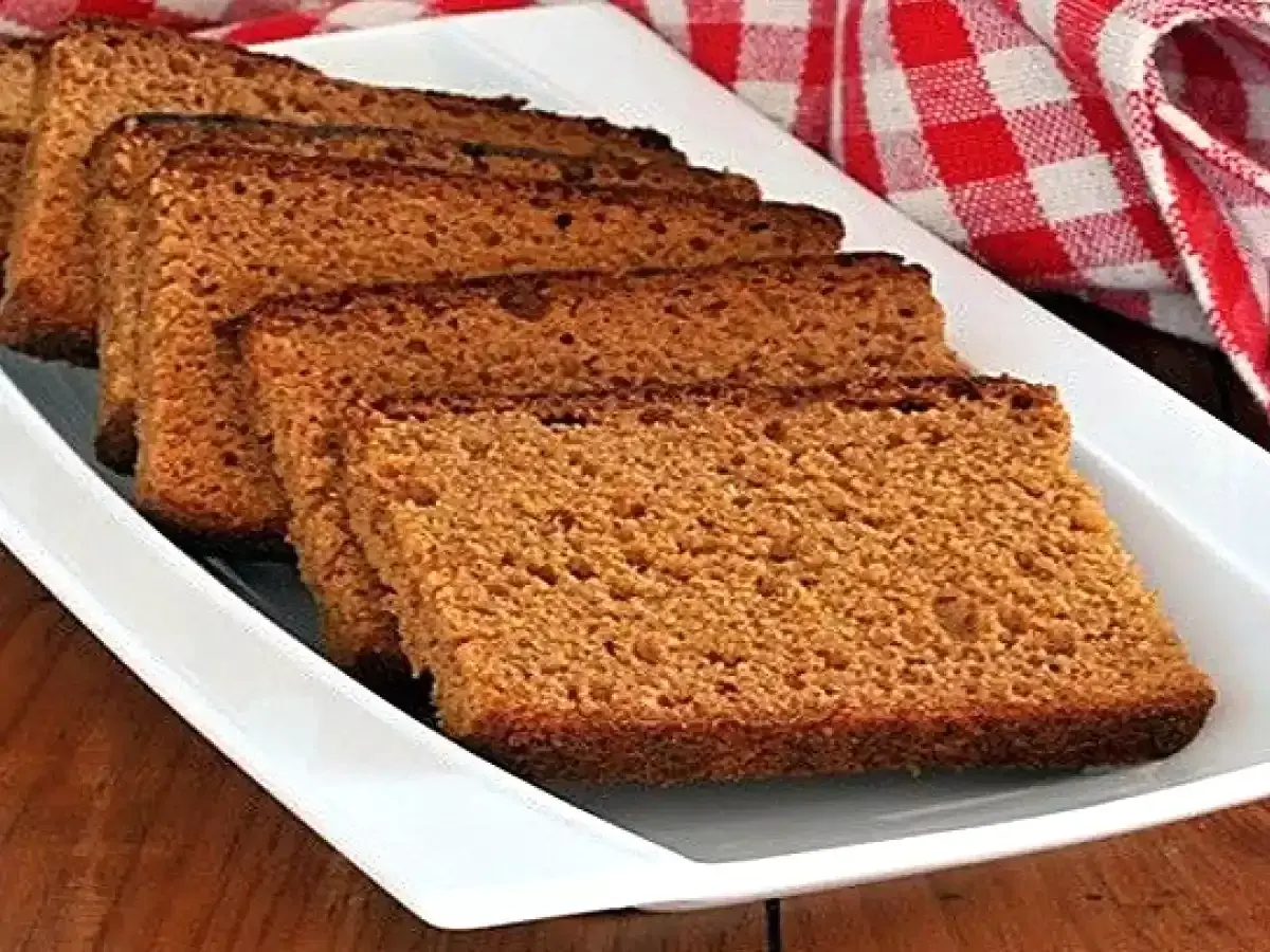 Tranches de pain d'épices moelleux disposées sur un plat blanc, avec un torchon à carreaux rouges en arrière-plan.
