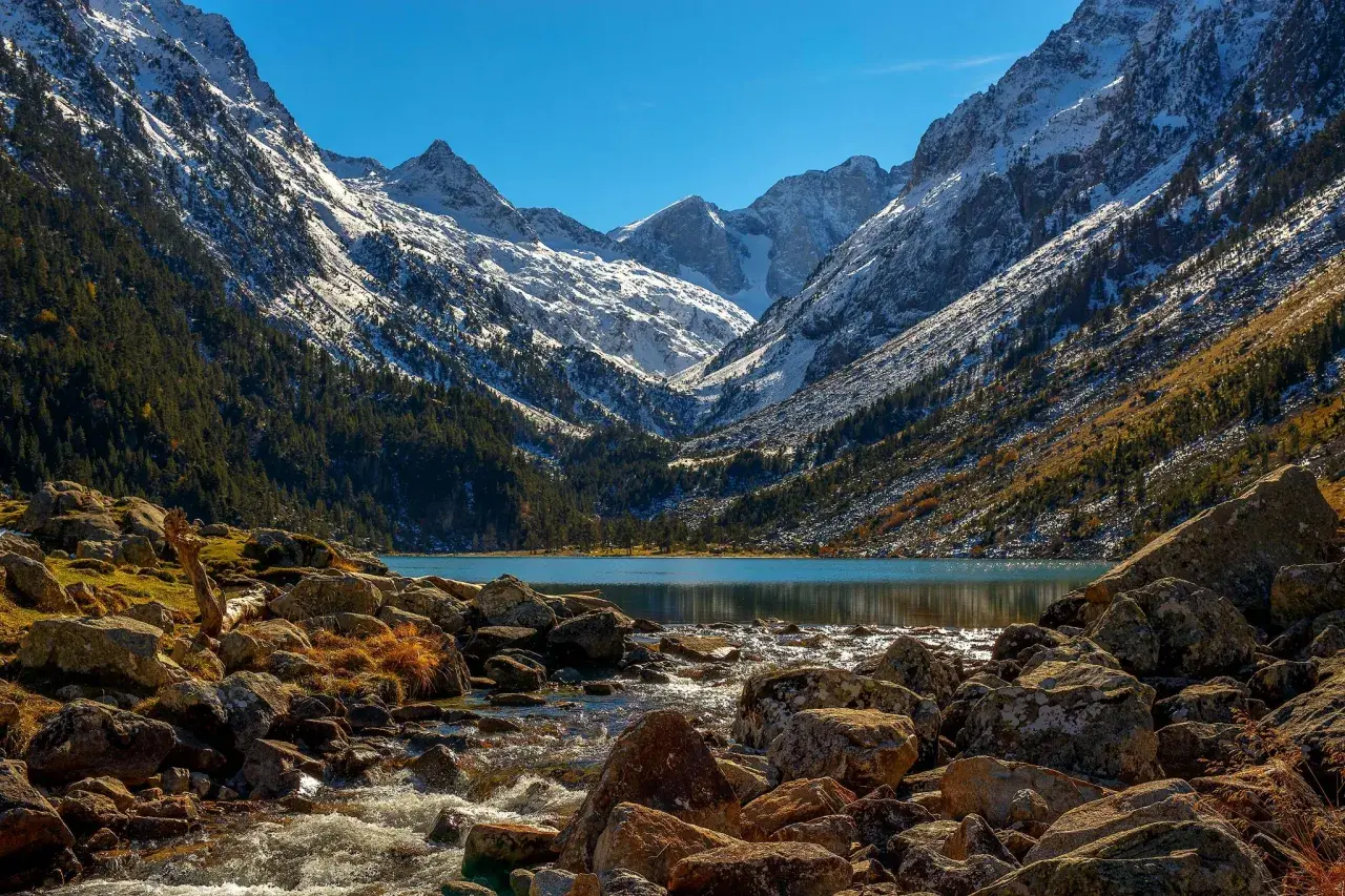 Majestuosas montañas nevadas flanquean el sereno lac de Gaube, con un arroyo rocoso que desemboca en sus aguas turquesas.