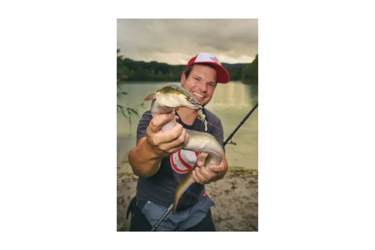Glücklicher Angler hält einen Aal, der an einer Fischfetzen-Montage hängt.