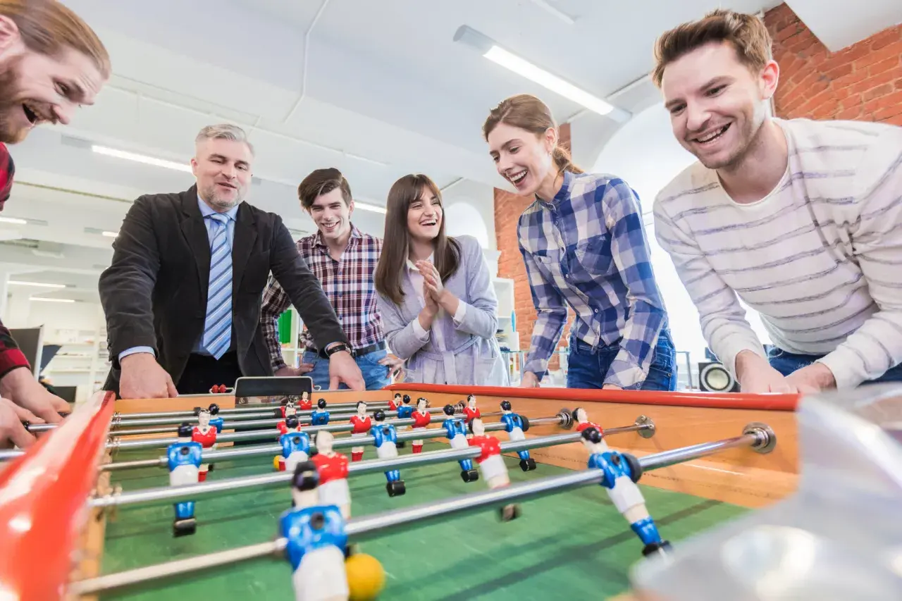 Colleagues laugh and play foosball, showcasing great employee engagement games.