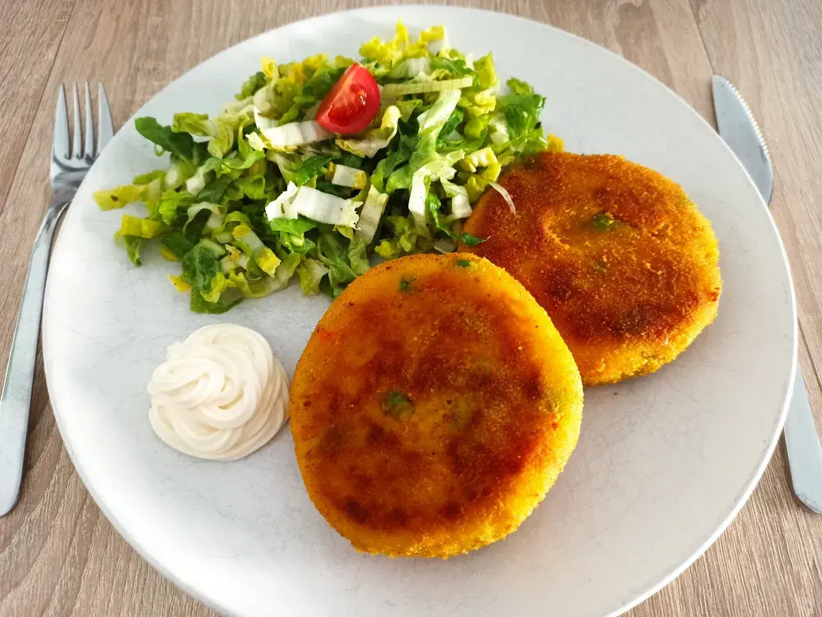 Zwei goldbraune, vegetarische Frikadellen mit einem frischen Salat und Mayonnaise auf einem Teller.