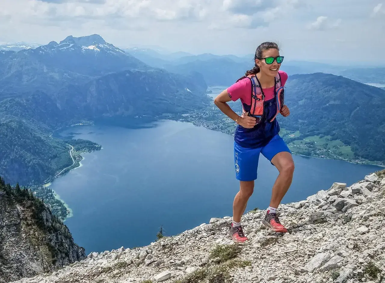 Läuferin im Gebirge, die zeigt, wie verbessere ich meine ausdauer durch anspruchsvolles Gelände. Bergsee und Gipfel im Hintergrund.