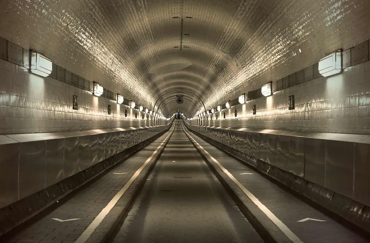Der lange, beleuchtete Gang des alten Elbtunnels mit seinen gekachelten Wänden und Lichtern, die eine Perspektive erzeugen.