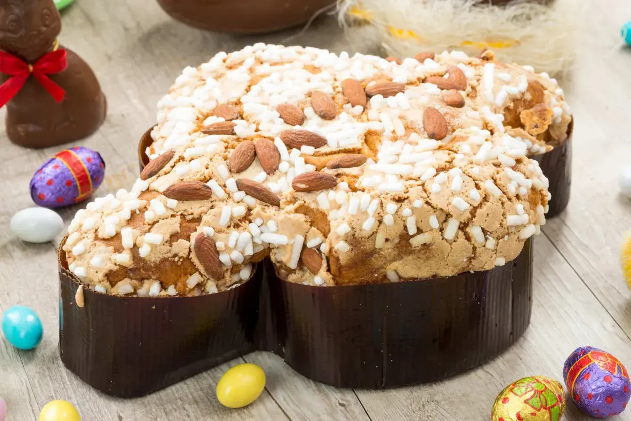 Colomba pasquale ricetta: dolce soffice con mandorle e glassa croccante, circondata da uova di cioccolato e coniglietti.
