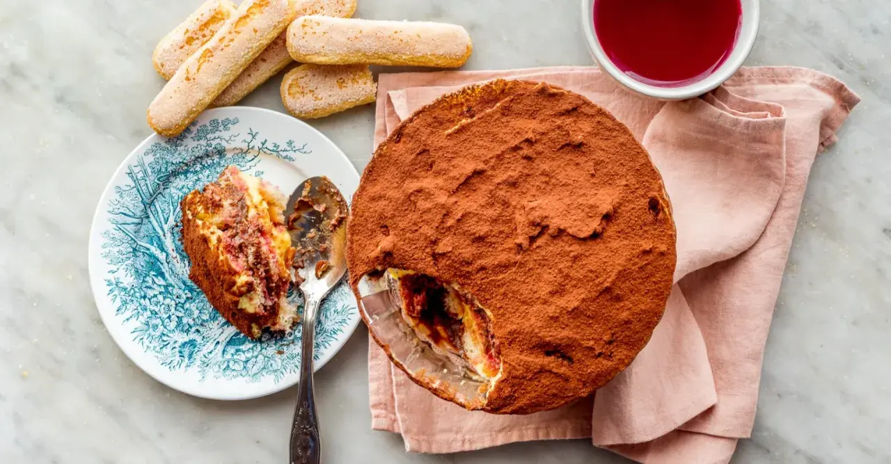 Délicieuse zuppa inglese recette, avec une part déjà servie sur une assiette ornée. Des biscuits à la cuillère et une coupelle de coulis complètent ce dessert gourmand.