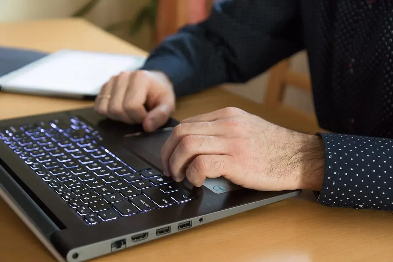 Dłonie pracują na laptopie z podświetlaną klawiaturą. Procesor AMD Ryzen 5 5600H zapewnia płynność pracy.