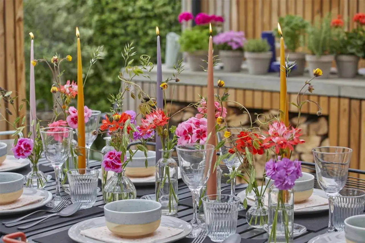 Tavola apparecchiata con candele colorate e fiori freschi, un'ispirazione per decorazioni estive fai da te.