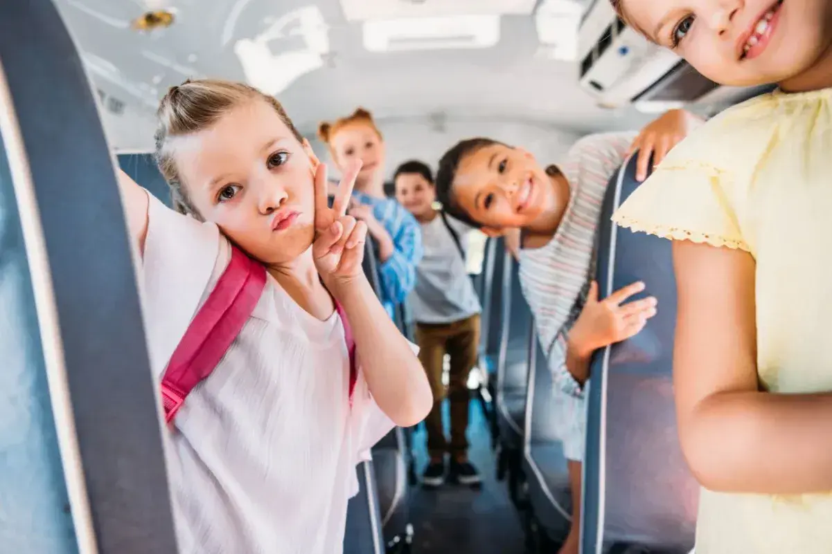 Dzieci w autobusie szkolnym robią sobie zdjęcie. Dziewczynka z przodu robi dziubek i znak pokoju. Wszyscy wyglądają na szczęśliwych, co świadczy o ich niekaralności na tle seksualnym.