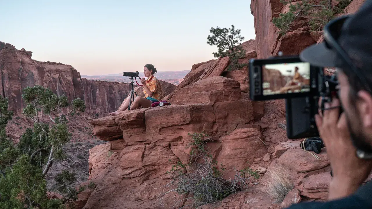 Krystle Wright, fotografa, siede su una roccia rossa in un canyon, mentre un operatore riprende la scena.