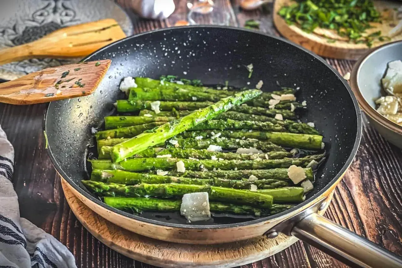Grüner Spargel wird in einer Pfanne mit Käse und Kräutern zubereitet. Ein köstliches Gericht, das zu vielen Spargel Rezepten passt.