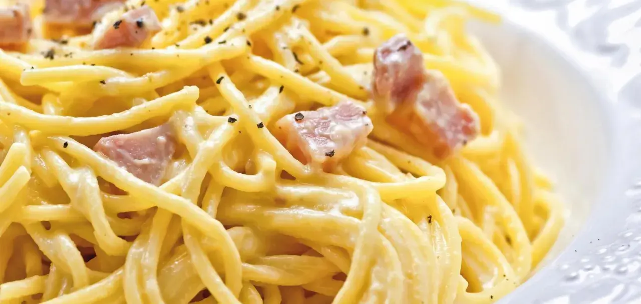 Ein Teller Spaghetti Carbonara, klassisch italienisch zubereitet mit cremiger Sauce und Speckwürfeln, bestreut mit schwarzem Pfeffer.