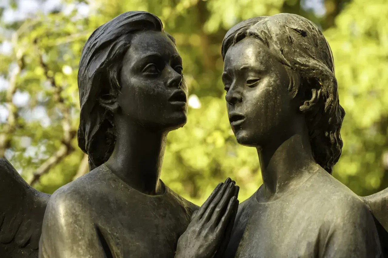 Deux anges en bronze, œuvre d'un fondeur d'art, se regardent tendrement. Leurs mains jointes évoquent une prière silencieuse.