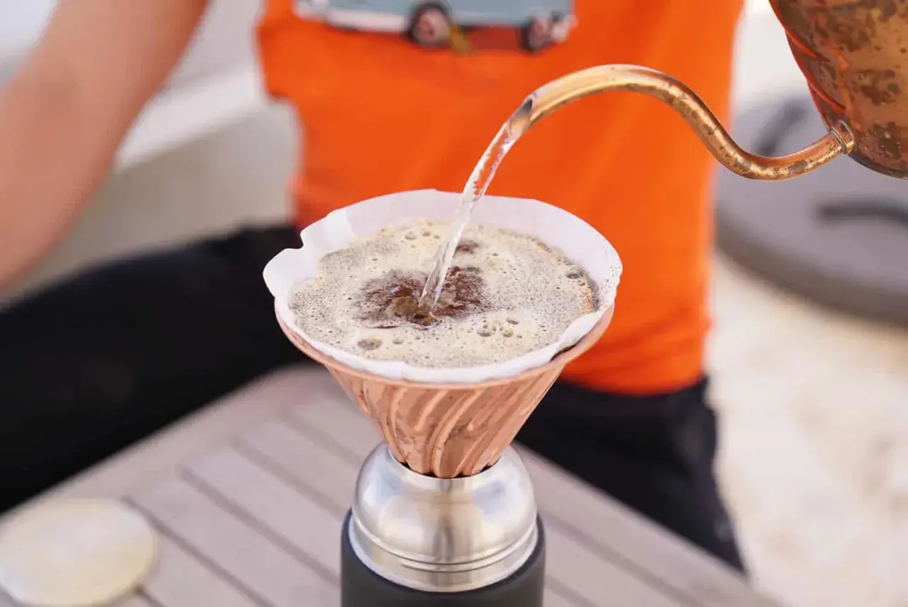 Heißes Wasser fließt aus einer Kupferkanne in einen Filter, um köstlichen Kaffee zu machen.
