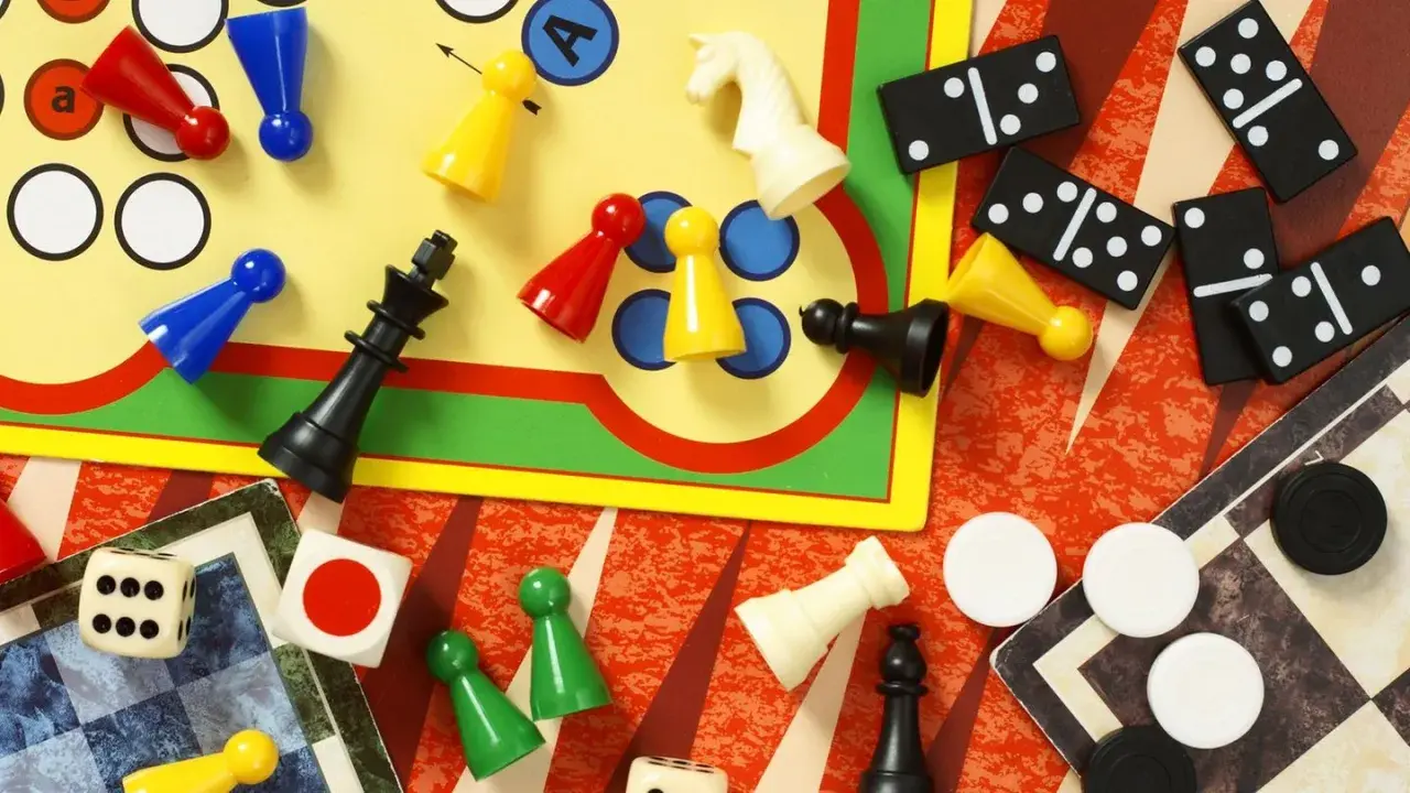 Bunte Spielfiguren, Würfel, Dominosteine und Schachfiguren liegen verstreut. Eine bunte Mischung bekannter Brettspiele für endlosen Spielspaß.