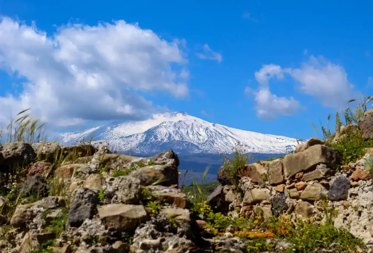 Rovine antiche incorniciano la maestosa vista dell'Etna innevato, un paesaggio iconico di Taormina.
