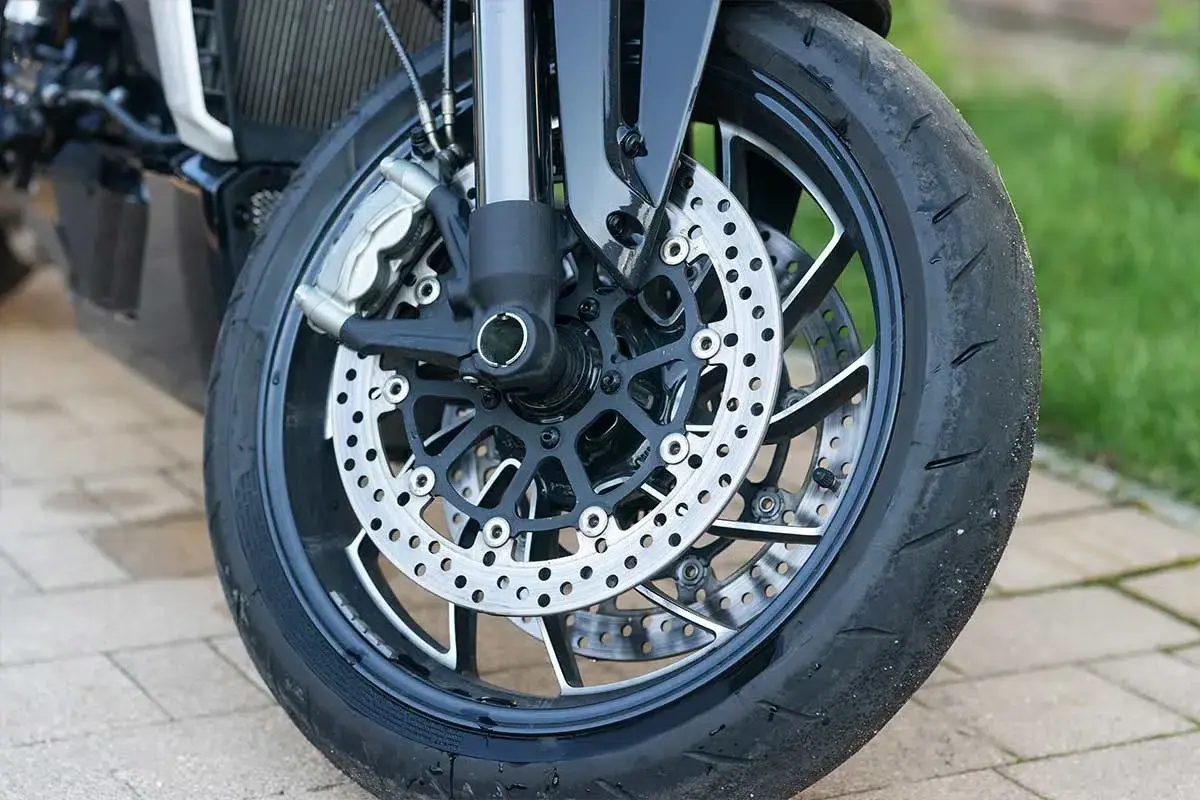 Rueda de moto con disco de freno perforado y pinza. Parece que hay un pinchazo lateral en la rueda, listo para ser reparado.
