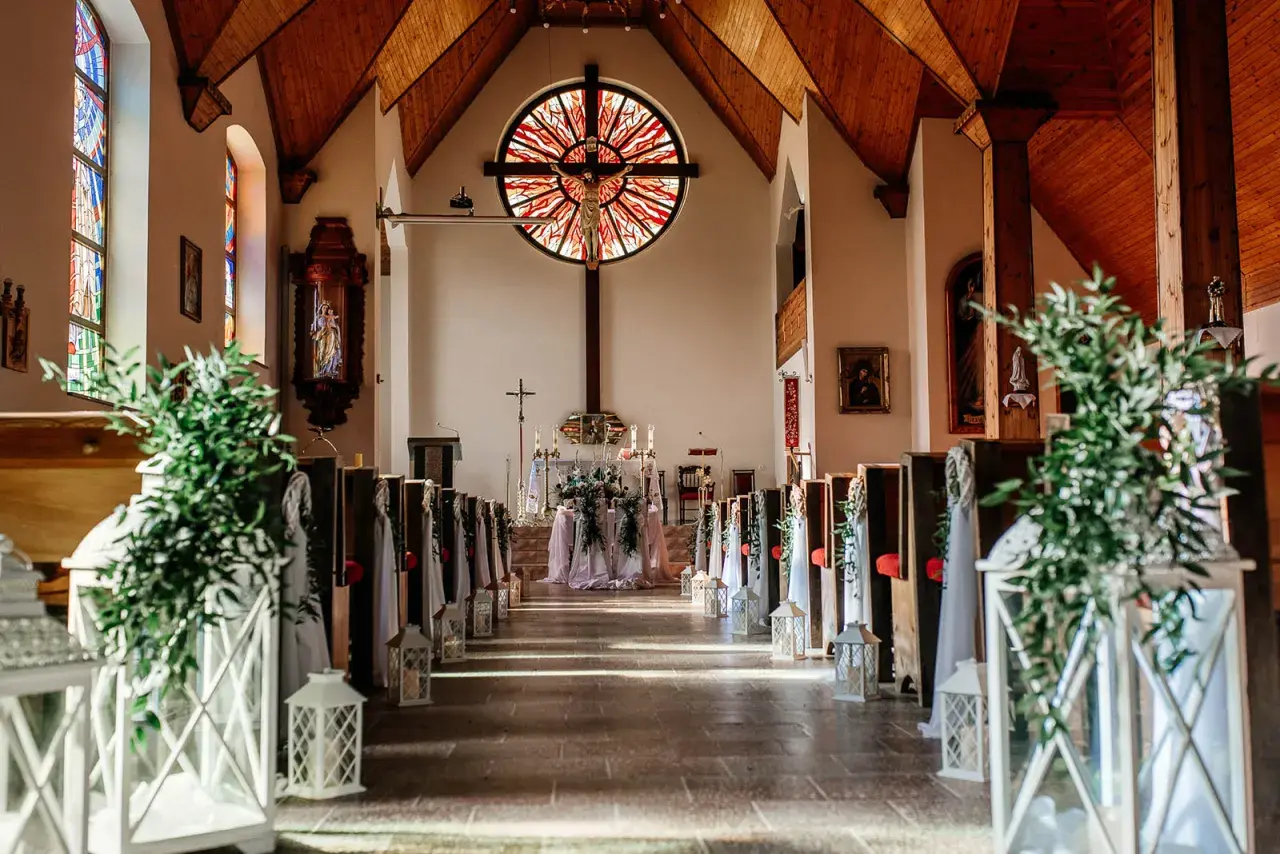 Piękna dekoracja kościoła na ślub samemu: ławki ozdobione zielenią i lampionami, ołtarz z kwiatami.