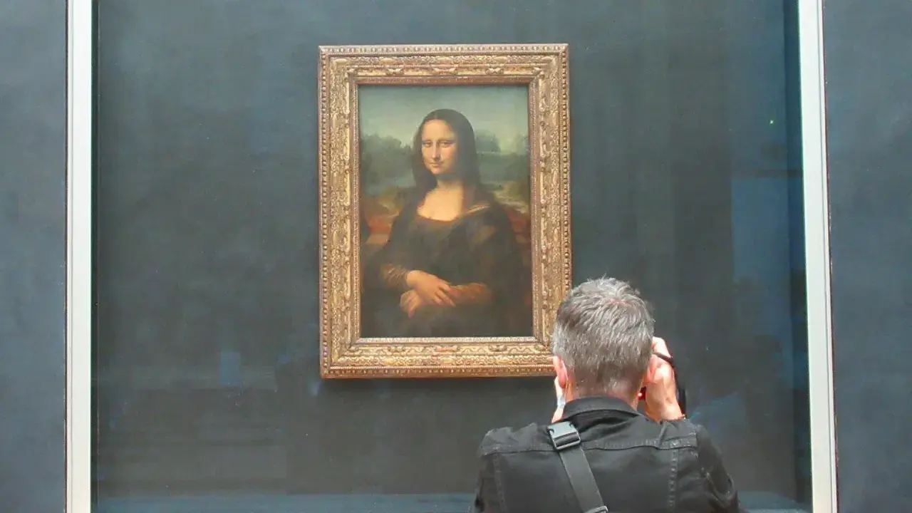 Ein Mann fotografiert die Mona Lisa. Die Frage, wie lange hat Da Vinci für die Mona Lisa gebraucht, beschäftigt viele Besucher.