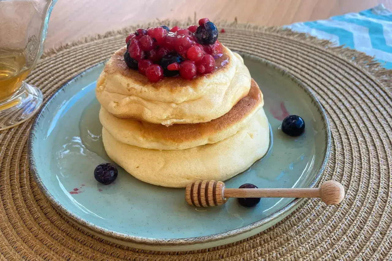 Pancake ricetta: soffici pancake impilati, guarniti con frutti di bosco e miele, pronti per essere gustati.