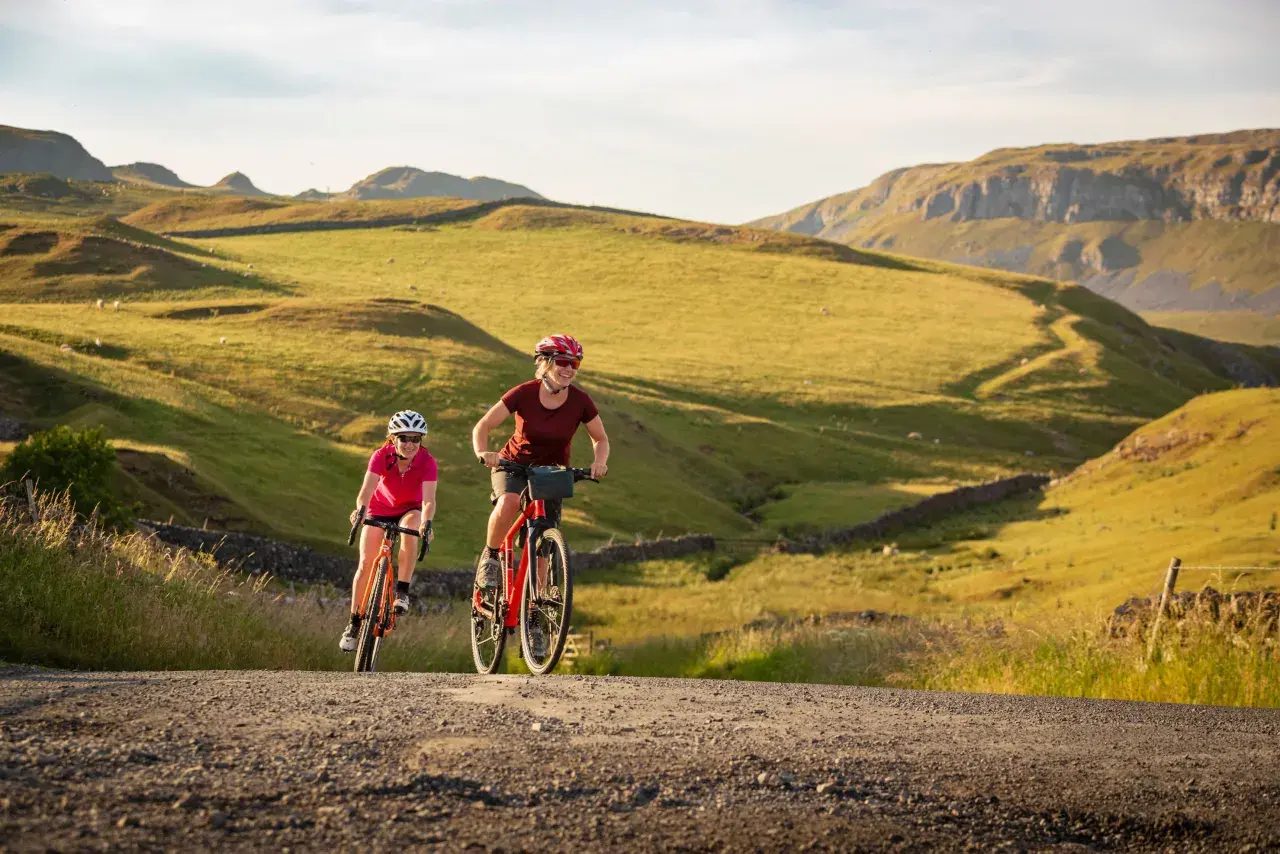 Two women enjoy a scenic ride on their bikes through rolling green hills, a perfect example of England bike tours.