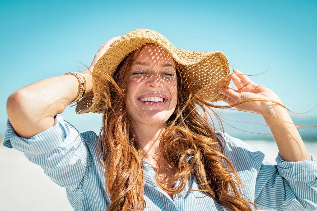 Mujer sonríe bajo sombrero de paja, con el pelo suelto. Consejos para como cuidar el pelo en verano.